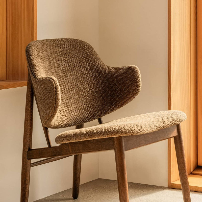 The Penguin Wooden Lounge Chair, fully upholstered in Logan Nutmeg fabric, styled in a minimalist interior corner.