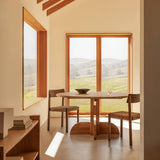 Oak Puffin Dining Table and Mauro Dining Chairs in a sunlit room with Crescent Shelving and views of rolling green hills.