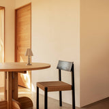 Black Mauro Dining Chair with a paper cord seat beside a Puffin Dining Table and Admiral Portable Table Lamp.