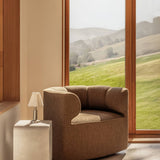 Eave Seamline Lounge Chair in Nutmeg fabric beside a Volume Side Table and Admiral Lamp with a scenic green hill view.