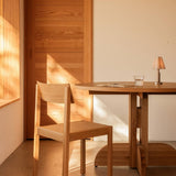 Solid oak Puffin Dining Table and Mauro Dining Chair in a sunlit interior with an Admiral Portable Table Lamp.