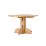 Puffin Dining Table, Round, in natural oak with a sculptural solid wood base, shown at an angle against a white background.
