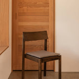 Dark stained oak Mauro Dining Chair featuring a striped seat cushion, set against a light wood panelled sliding door.