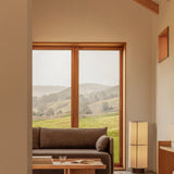 Natural oak Conrad Lounge Table and Offset Sofa in a bright room with a Hashira Floor Lamp and scenic window views.